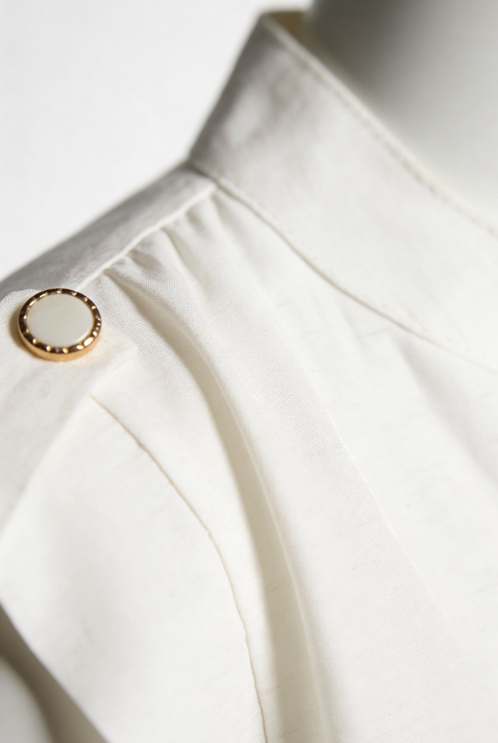 Blusa de dama moda con detalle de botón dorado sobre tela blanca elegante.