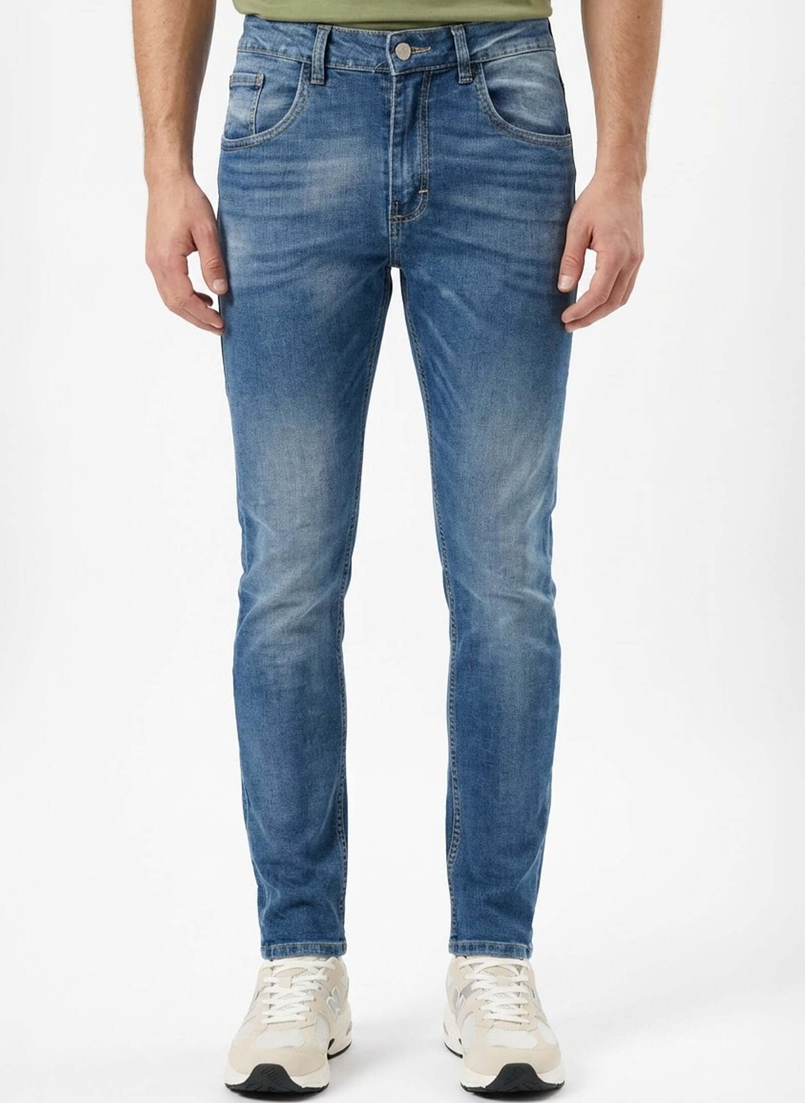 Jean de hombre básico en jeans azules con camiseta verde y zapatillas blancas.
