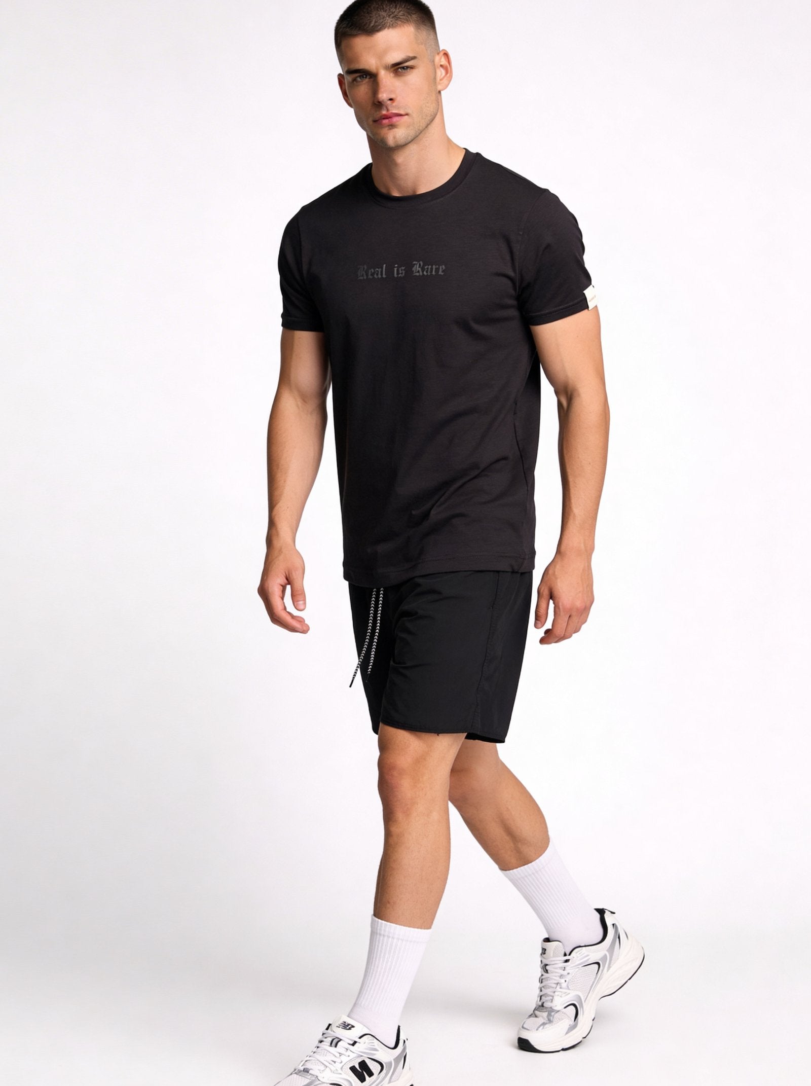 Camiseta de hombre sublimada en color negro, modelo masculino caminando con pantalones cortos deportivos.