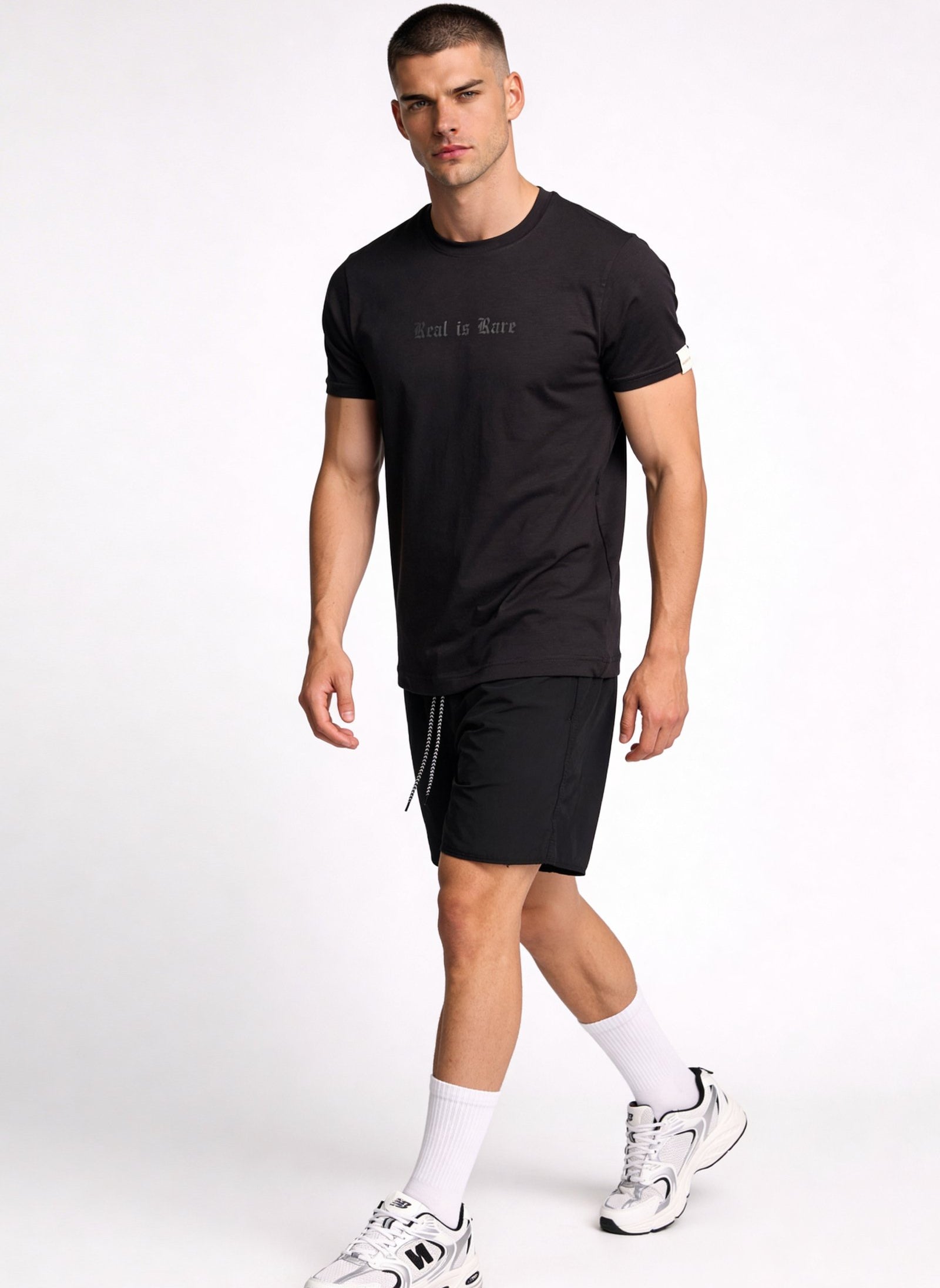 Camiseta de hombre sublimada en color negro, modelo masculino caminando con pantalones cortos deportivos.
