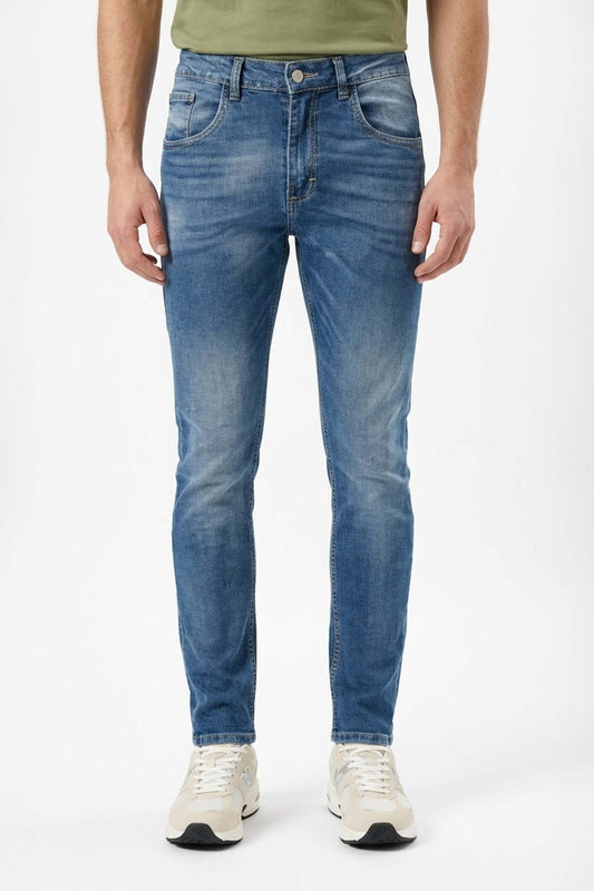 Jean de hombre básico en jeans azules con camiseta verde y zapatillas blancas.