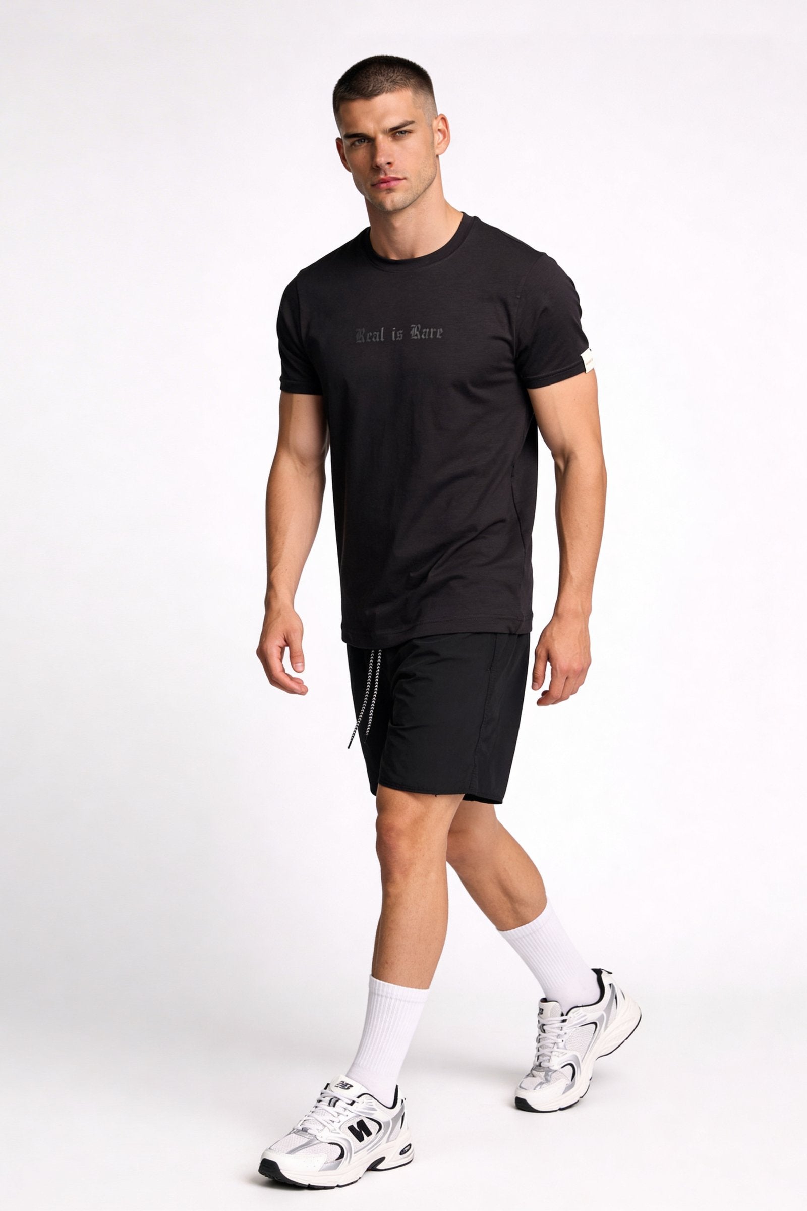 Camiseta de hombre sublimada en color negro, modelo masculino caminando con pantalones cortos deportivos.